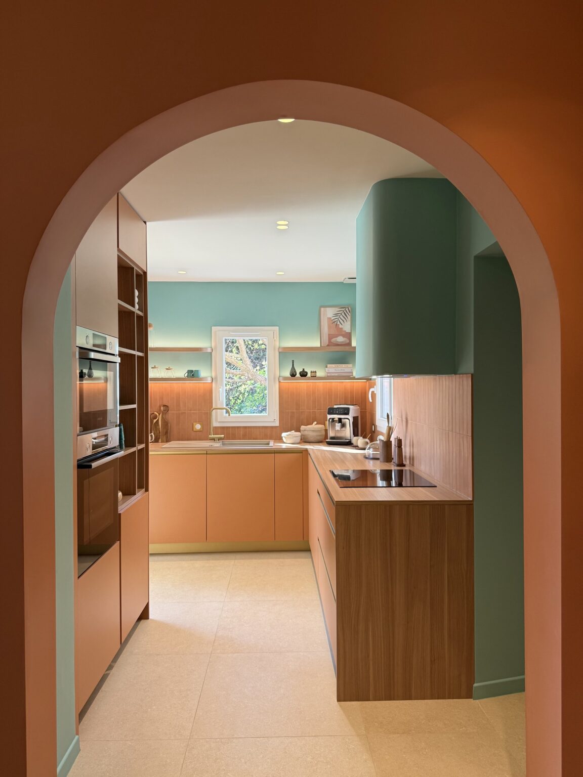 Vue sur la cuisine sur mesure à travers une arche terracotta – projet Favorita